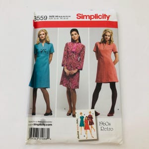 May include: Simplicity sewing pattern number 3559 for a 1960s Retro dress. The pattern includes three different dress styles: a turquoise dress with a bow, a pink and black paisley dress with a collar, and a coral dress with a collar. The pattern is for sizes H5 6, 8, 10, 12, and 14, which corresponds to European sizes 32-40 and French sizes 34-42.
