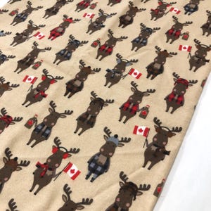 May include: Beige fabric featuring a repeating pattern of cartoon moose. The moose are brown with black antlers and wear plaid scarves and hats, and hold Canadian flags and maple syrup bottles.