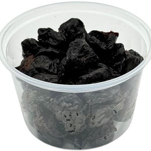May include: A clear plastic container filled with dark, dried plums. The plums are a deep, purplish-black color and appear wrinkled. The container is round with a slightly flared rim, and the background is plain white.