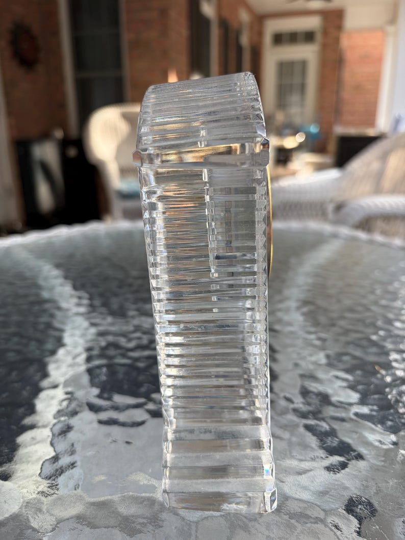 K&ouml;nnte beinhalten: Eine klare, rechteckige Kristallflasche mit horizontalen Rillen. Die Flasche hat ein goldfarbenes Band um den oberen Rand. Die Flasche steht auf einem Glastisch.
