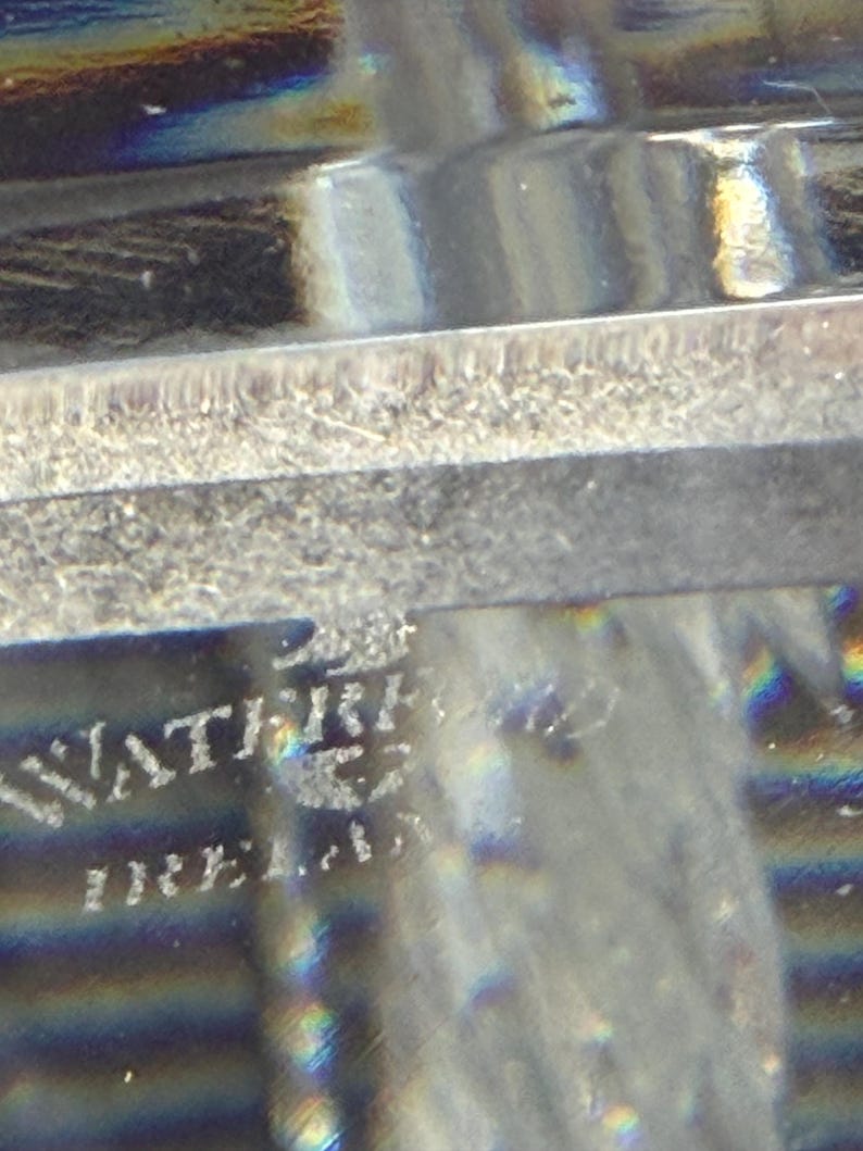 K&ouml;nnte beinhalten: Nahaufnahme eines transparenten Glasobjekts mit dem eingravierten Text "WATERFORD IRELAND". Das Glas hat eine strukturierte Oberfl&auml;che und reflektiert das Licht, wodurch ein Regenbogeneffekt entsteht. Das Objekt scheint ein dekoratives St&uuml;ck zu sein.