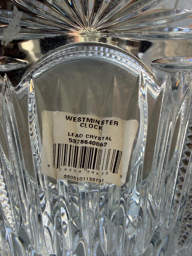 K&ouml;nnte beinhalten: Nahaufnahme eines transparenten Bleikristallobjekts mit strukturiertem, geometrischem Design. Ein Etikett lautet "Westminster Clock" und "Lead Crystal". Das Etikett enth&auml;lt auch einen Barcode und Seriennummern. Das Kristall reflektiert Licht.