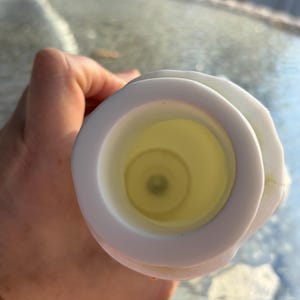 May include: A white candle holder with a circular design. The interior is a pale yellow color. The candle holder is being held by a person.