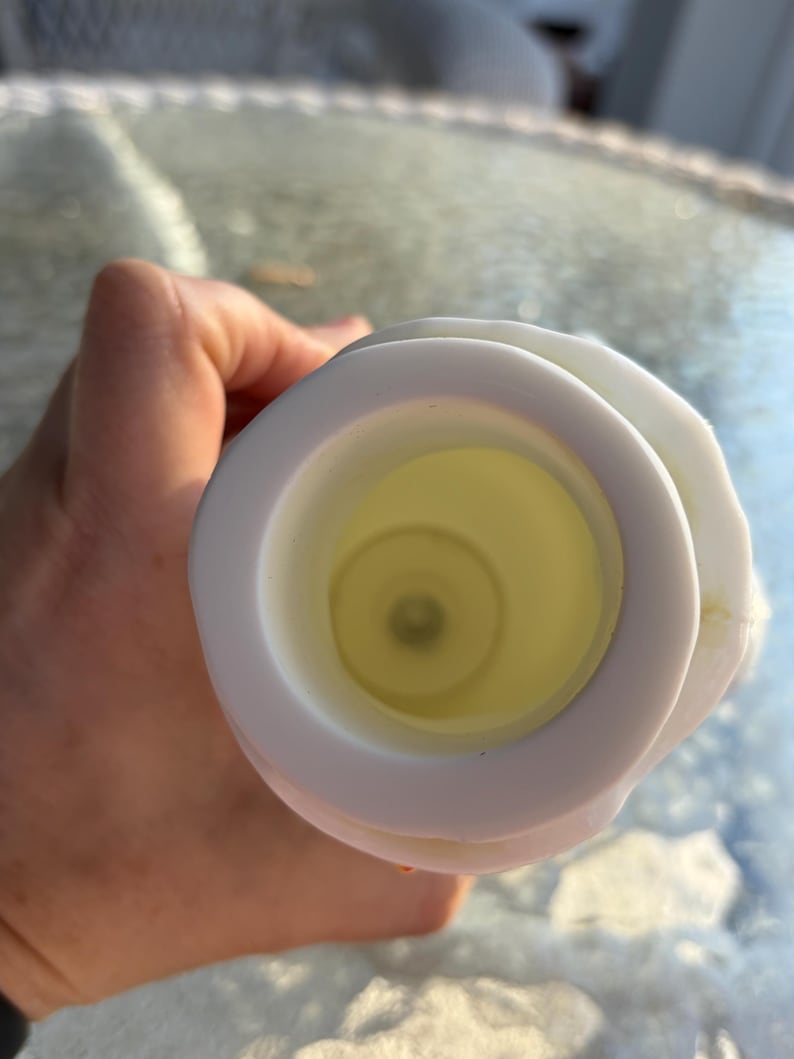 May include: A white candle holder with a circular design. The interior is a pale yellow color. The candle holder is being held by a person.