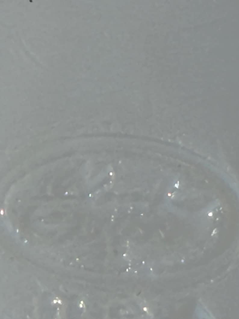 May include: Close-up of a clear, textured glass object with an oval shape. The glass has a slightly frosted appearance and reflects light, creating small, bright highlights. The object appears to be part of a larger glass item.