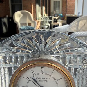 K&ouml;nnte beinhalten: Eine transparente Waterford Crystal-Uhr mit goldfarbener L&uuml;nette und r&ouml;mischen Ziffern. Das Zifferblatt zeigt "WATERFORD CRYSTAL". Die Uhr befindet sich vor einem verschwommenen Hintergrund im Freien.