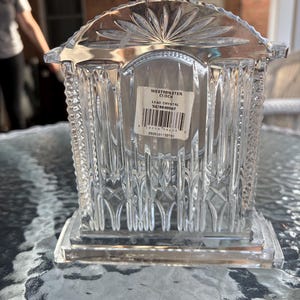 K&ouml;nnte beinhalten: Eine transparente Westminster-Uhr aus Bleikristall mit rechteckigem Sockel und dekorativer Oberseite. Die Uhr hat vertikale und geometrische Muster. Auf dem Etikett steht "Westminster Clock" und "Lead Crystal".