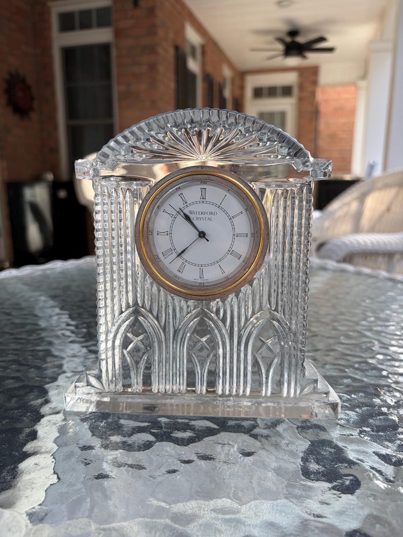 K&ouml;nnte beinhalten: Eine klare Kristalluhr mit goldfarbenem Rahmen und wei&szlig;em Zifferblatt. Die Uhr hat r&ouml;mische Ziffern und die Worte "WATERFORD CRYSTAL" auf dem Zifferblatt. Die Uhr ist rechteckig mit gew&ouml;lbter Oberseite.