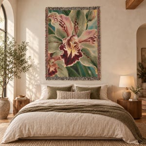 May include: A rectangular woven wall tapestry featuring a large, detailed orchid flower in shades of pale green, soft pink, and deep maroon. The floral design is set against a teal background, and the tapestry has a decorative fringed edge.