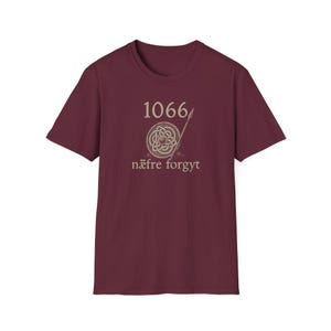 May include: Burgundy t-shirt with the number "1066" above a Celtic knot design and spear. The text "nāfre forgyt" is below. The shirt is a solid colour.