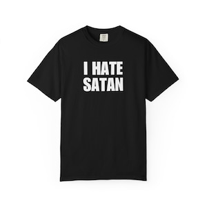 May include: A black short-sleeved t-shirt featuring the white text I HATE SATAN printed in a bold, sans-serif font across the chest. The garment has a crew neckline and a standard fit, with a small brand label visible inside the collar area.