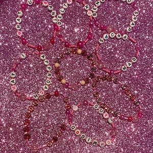 May include: Five pink beaded bracelets with letter beads spelling out the words "WHAT U WANT", "DELTA", "BE KIND", "PROPS", and "MAD".