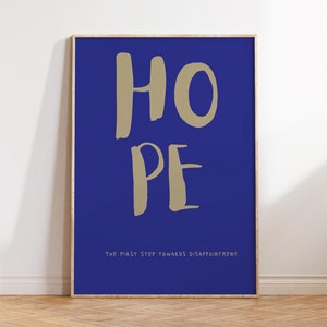 May include: A framed print with a blue background and the word "HOPE" written in a large, stylized font in beige. The text below the word "HOPE" reads "THE FIRST STEP TOWARDS DISAPPOINTMENT."