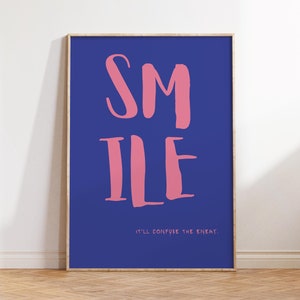 May include: A framed poster with a blue background and pink text that reads "SMILE it'll confuse the enemy."