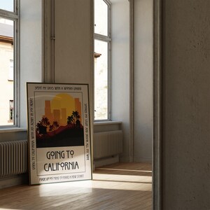 May include: A framed poster with the text "Going to California" and a sunset graphic with palm trees and city silhouettes. The poster is leaning against a wall near a window, with the text "Spent my days with a woman unwind" and "Smoked my stuff and drank all my wine".