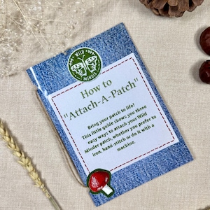 Puede incluir: Una etiqueta con textura de mezclilla con el texto "How to Attach-A-Patch" y un parche en forma de hongo. La etiqueta incluye instrucciones sobre cómo colocar parches con plancha, coser a mano o a máquina. El logotipo de Wild Minder está en la parte superior.