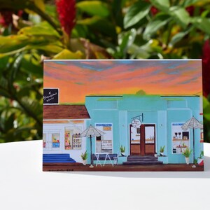 May include: A painting of a turquoise building with two storefronts. The building has a sign that reads "The Lemonade Stand". The building is set against a sunset sky with pink, orange, and yellow clouds.