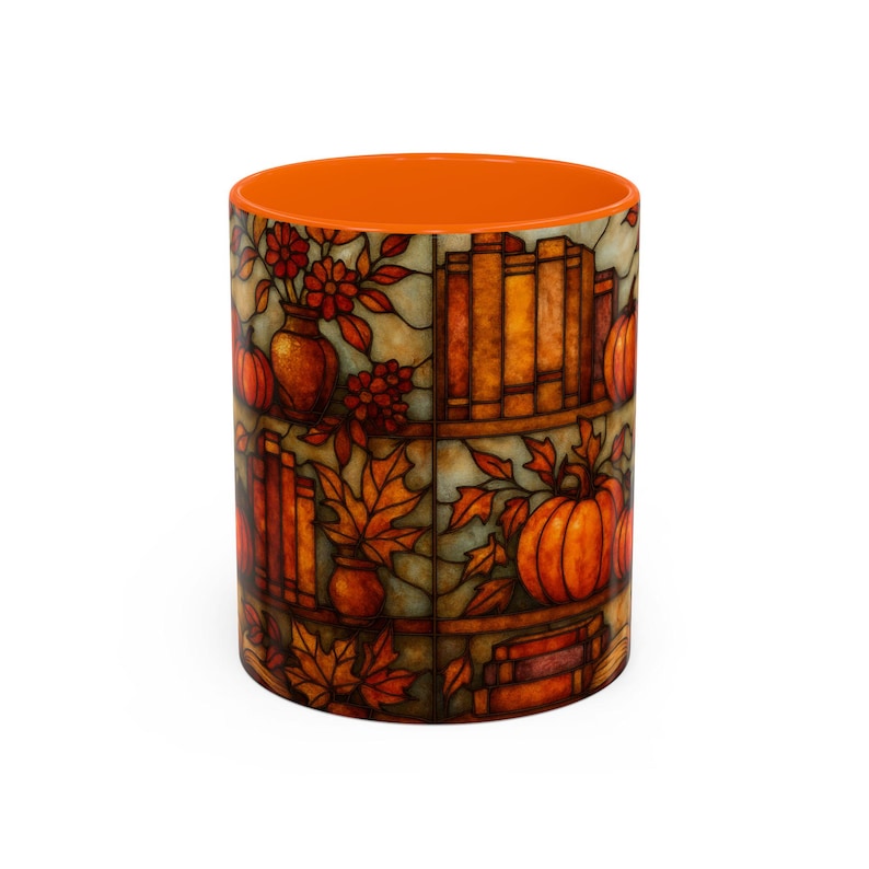 May include: A ceramic mug with an orange interior and a stained-glass design featuring pumpkins, books, fall leaves, and flowers in shades of orange, brown, and yellow. The mug has a cylindrical shape.