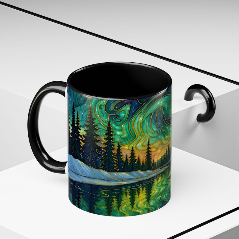 May include: A black-handled coffee mug with a vibrant landscape design. The artwork features a forest, lake, and swirling aurora borealis in shades of green, blue, and gold. The interior of the mug is black.