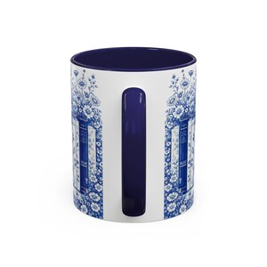 May include: White ceramic mug with a navy blue interior and handle. The exterior features a blue and white floral and book design. The design includes the word "NOW" on the side of the mug. A decorative and functional item for beverages.