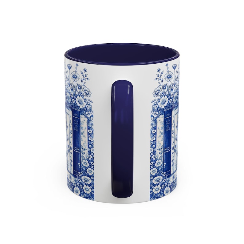 May include: White ceramic mug with a navy blue interior and handle. The exterior features a blue and white floral and book design. The design includes the word "NOW" on the side of the mug. A decorative and functional item for beverages.
