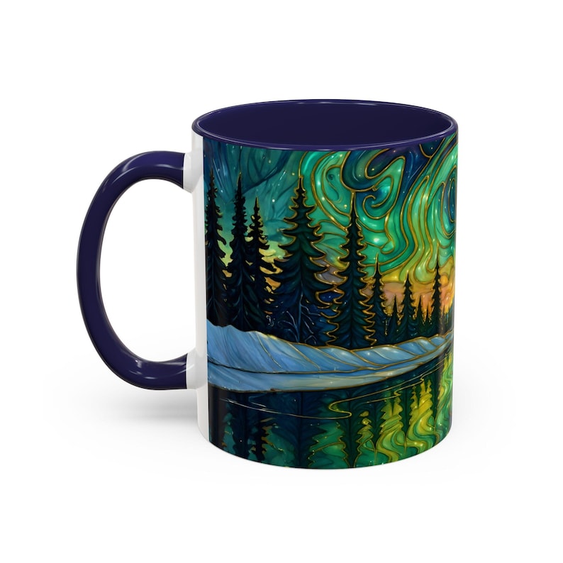 May include: A white ceramic coffee mug with a dark blue handle and interior. The mug features a vibrant illustration of a forest scene with a lake reflecting the aurora borealis in shades of green, gold, and blue.