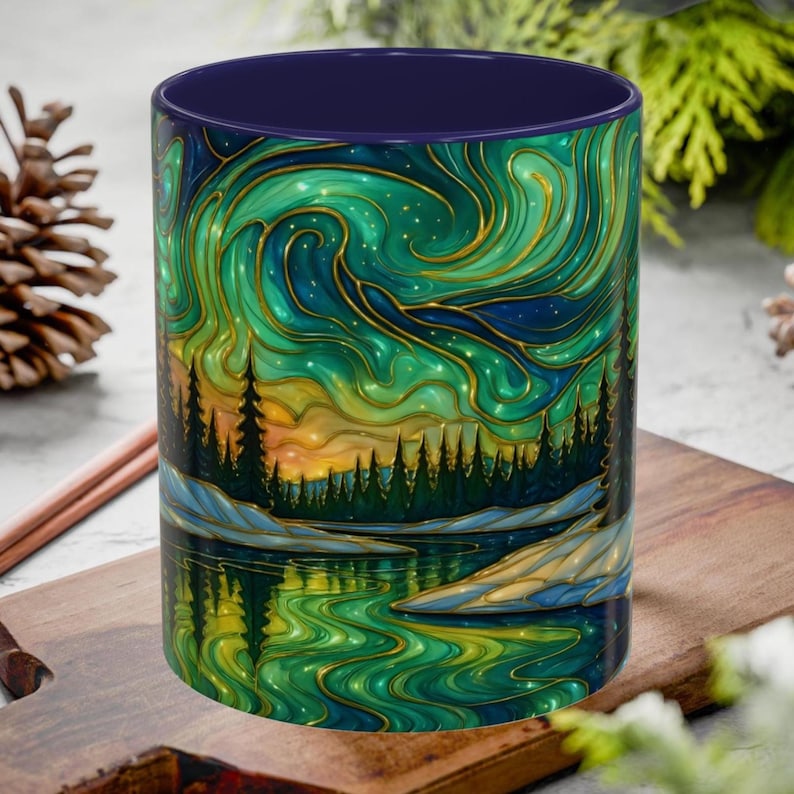 May include: A ceramic mug with a vibrant landscape design. The artwork features a green and blue aurora borealis over a forest and lake scene. The mug has a dark blue interior and a gold outline on the design.