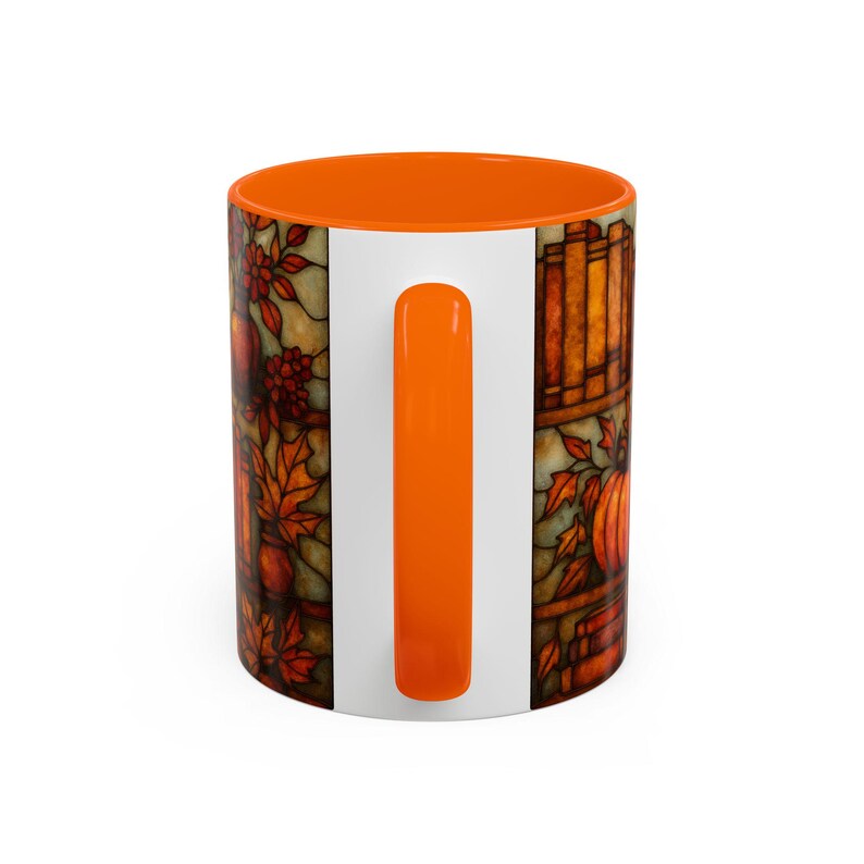 May include: A white ceramic mug with an orange interior and handle. The mug features a stained-glass style design with fall leaves, pumpkins, and a stack of books. The design is in shades of orange, brown, and yellow.