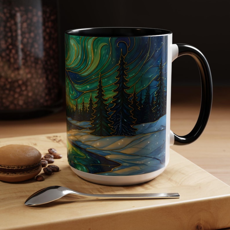 May include: White ceramic mug with a black interior and handle. The mug features a colorful illustration of a winter landscape with a forest and aurora borealis in shades of green, blue, and gold. The mug is on a wooden surface.