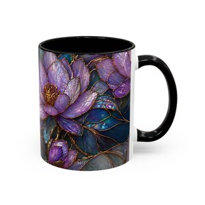 May include: White ceramic coffee mug with a black interior and handle. The mug features a floral design with purple, blue, and gold accents. The flowers are stylized with a stained glass effect.