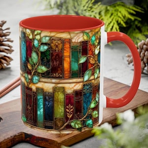May include: A ceramic mug with a bright red interior and handle, featuring a wrap-around design of colorful, stained-glass style book spines arranged on shelves, accented with green leafy vines that climb across the vertical book rows.