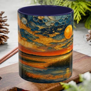 May include: A cylindrical ceramic mug featuring a vibrant, stained-glass style landscape print. The design depicts a sunset over a body of water with golden clouds, a bright yellow sun, and dark blue tones. The interior of the mug is a solid dark blue.