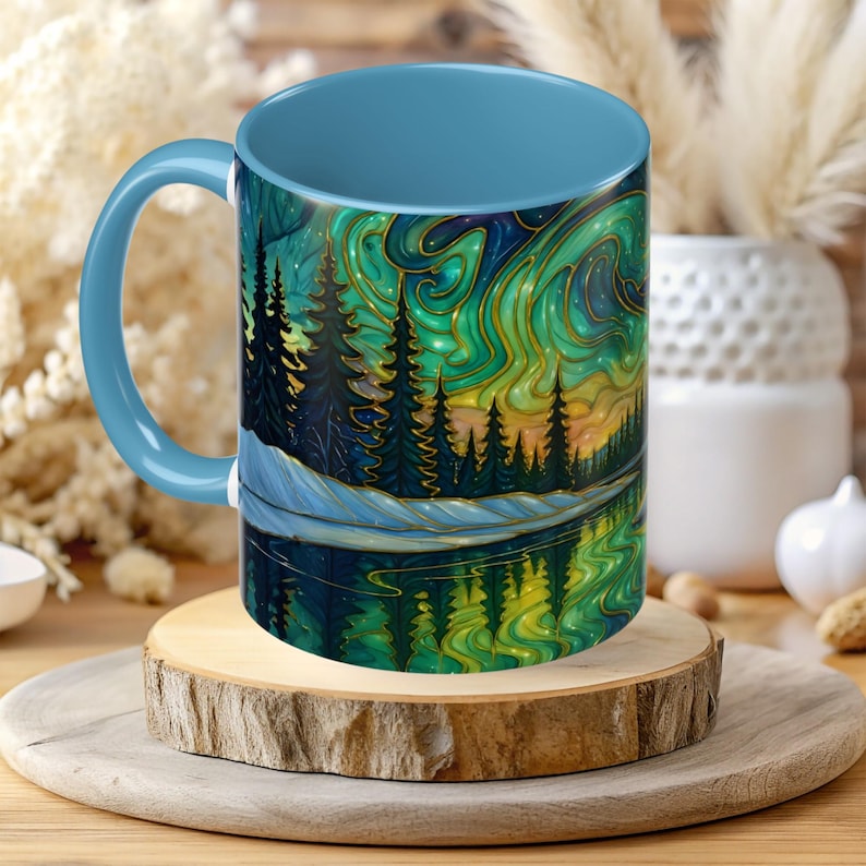 May include: A ceramic mug with a light blue handle and interior. The exterior features a landscape design with a forest, lake, and a colorful sky with green and gold accents. The mug sits on a wooden coaster.