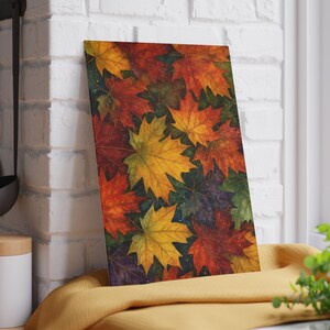 May include: A rectangular cutting board featuring a vibrant autumn leaf design. The leaves are in shades of red, orange, yellow, and green, creating a colorful and seasonal aesthetic. The board is leaning against a white brick wall.