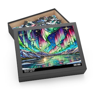 May include: A 500 piece jigsaw puzzle featuring a stained glass style image of the Northern Lights reflected in a lake. The box is black with the text "16x20 Puzzle 500 pcs Ages 9+"