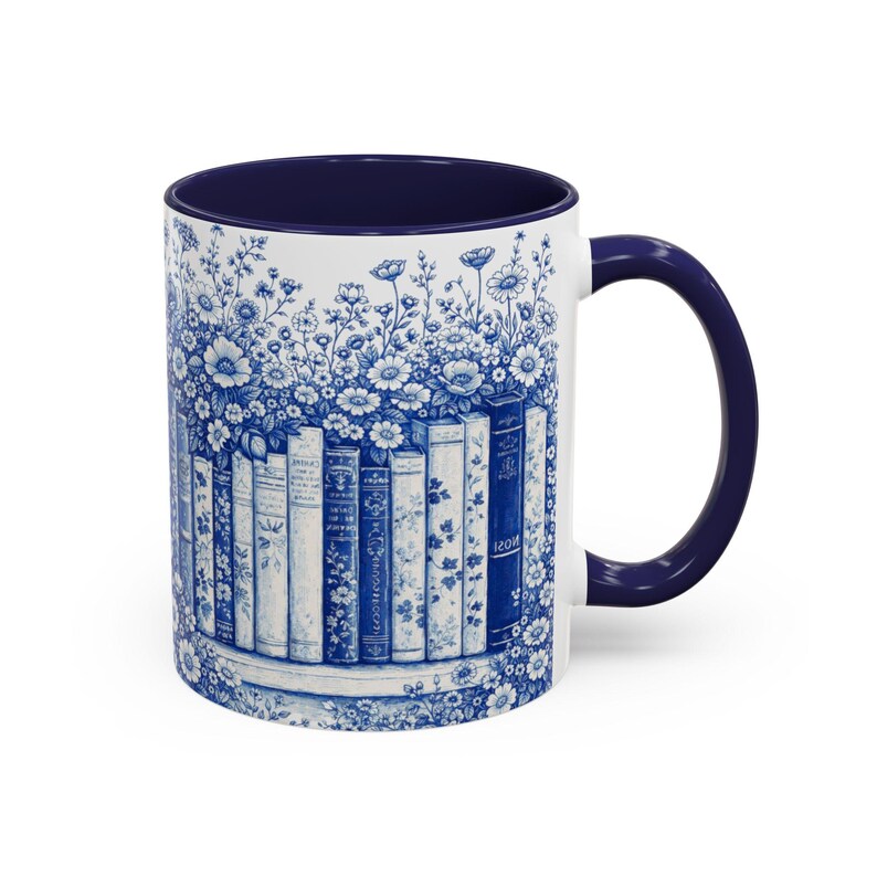 May include: White ceramic mug with a blue interior and handle. The mug features a blue and white floral design with a row of books. The design wraps around the mug, creating a cohesive and decorative look.