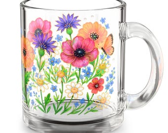 May include: Clear glass mug decorated with a vibrant floral design. The artwork features pink, orange, and purple flowers, along with a butterfly, set against a white background. The mug has a clear handle and a simple, elegant shape.