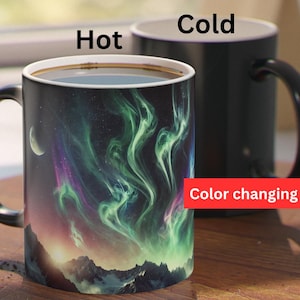 May include: A black color-changing mug with a design of a starry sky with green and purple aurora borealis. The mug reads "Hot" and "Cold" on the sides and "Color changing mug" at the bottom.