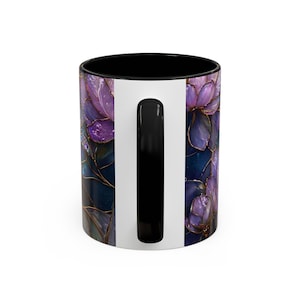 May include: A ceramic coffee mug with a black interior and handle. The exterior features a floral design in shades of purple and gold against a dark blue background. A white vertical stripe runs down the side of the mug.