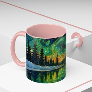 May include: A ceramic mug with a pink handle and interior. The exterior features a vibrant landscape painting with a forest, lake, and swirling green and gold sky. The design is reflected in the water.
