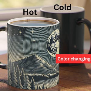 May include: A black color-changing mug with a white design of a mountain range, moon, and stars. The mug changes color when hot or cold. "Hot" and "Cold" are written on the mug. "Color changing mug" is written on the bottom of the mug.