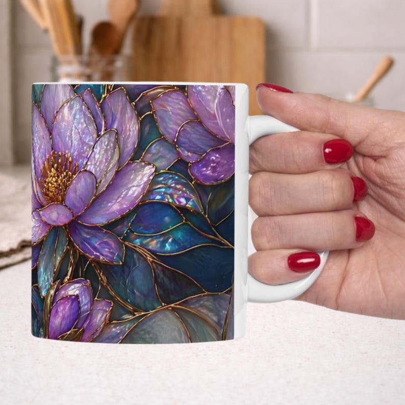 May include: White ceramic mug featuring a floral design with purple and blue hues. The design includes detailed illustrations of flowers and leaves with gold outlines, creating a stained-glass effect. The mug has a white handle.