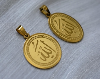 May include: Two gold-colored pendants with the Arabic inscription for "Allah". The pendants are oval and circular, with a decorative border. They have a loop for a chain and rest on a light gray, textured surface.