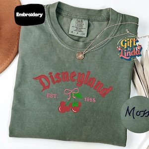 a green t-shirt with a Disneyland logo, a necklace, and a hat, all placed on a white surface.