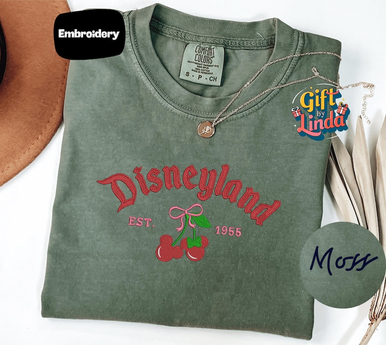 a green t-shirt with a Disneyland logo, a necklace, and a hat, all placed on a white surface.