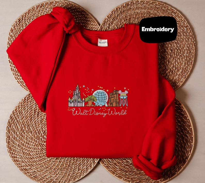 A red t-shirt with a graphic design of Disney landmarks and the text "Walt Disney World" printed on it, placed on a woven placemat.