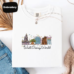 A white t-shirt with a graphic design of Disney World landmarks, including a castle, roller coaster, and globe, along with the text "Walt Disney World".
