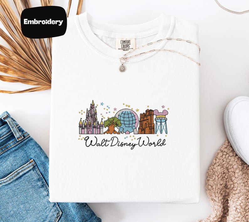 A white t-shirt with a graphic design of Disney World landmarks, including a castle, roller coaster, and globe, along with the text "Walt Disney World".