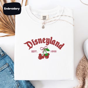 a white t-shirt with a Disneyland logo, a pair of blue jeans, and some decorative elements such as a leaf and a heart.