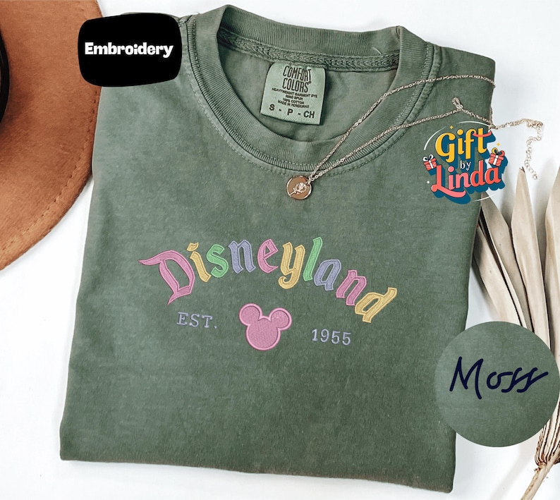 a green t-shirt with a Disneyland logo, a necklace, and a hat, all placed on a white surface.